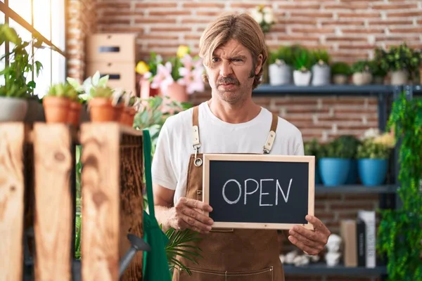 Caucasian man with mustache working at florist holding open sign skeptic and nervous, frowning upset because of problem. negative person.