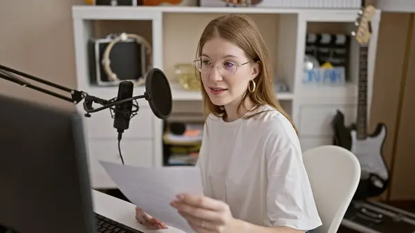 Young blonde woman radio reporter reading paper speaking on a show at radio studio