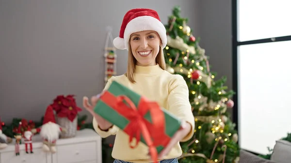 年轻的金发女人拿着礼物站在家里的圣诞树旁 — 图库照片