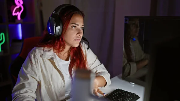 集中した若い赤毛の女性ストリーマー 激しいゲームセッション 深刻な仮想フェイスオフ ヘッドセットで 彼女の家のゲームルームの屋内で暗く明るくカプセル化 — ストック写真