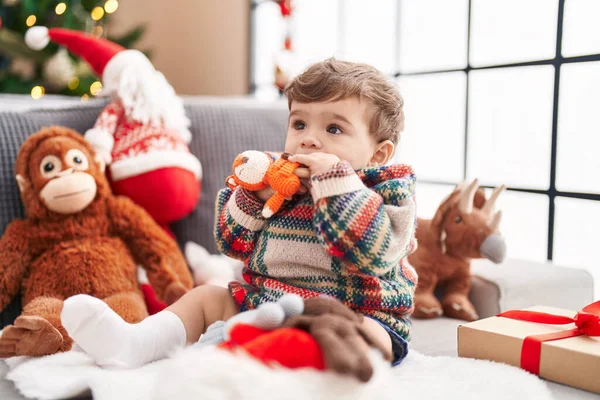 自宅でクリスマスツリーでソファーに座っている人形を吸う愛らしいヒスパニックの幼児 — ストック写真