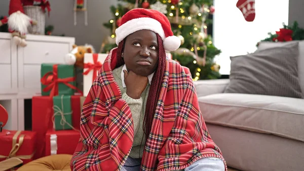 African woman with braided hair sitting on the floor by christmas tree looking upset at home
