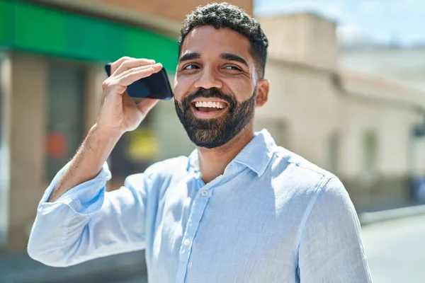 Young arab man miling confident listening audio message by the smartphone at street
