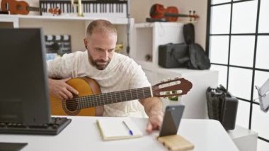 Yakışıklı beyaz erkek müzisyen müzik stüdyosunda klasik gitar dersine dalmış, zarif bir şekilde İspanyol akustik enstrüman çalıyor, gözleri akıllı telefon ekranında.