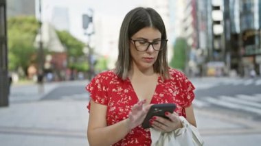 Tokyo 'da gözlüklü güzel İspanyol kadın. Şehir sokaklarında akıllı telefon aracılığıyla dijital bağlantı.