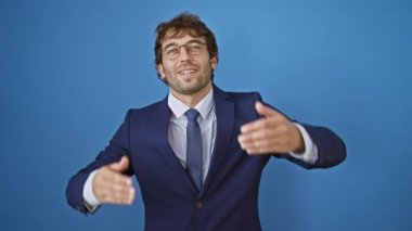 Neşeli, genç adam sevinçle elleri ile gözleri kaplayan, komik, kör bir oyunu ortaya koyuyor şık takım elbisesiyle, parlak mavi bir arka planda izole edilmiş