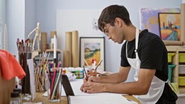 Çekici, genç İspanyol bir adam resim stüdyosuna hevesle resim çizer, akıllı telefonuna dalmış, fırçalar ve boya paletiyle çevrelenmiş.