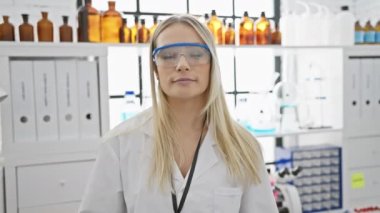 Kendine güvenen genç sarışın bilim kadını laboratuardaki başarılı bir deneyden sonra neşeyle gözlüklerini çıkarıyor.