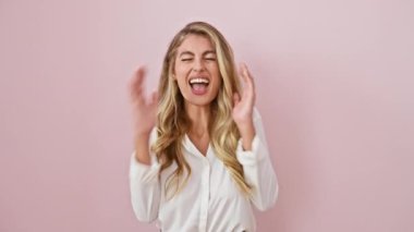 Neşeli genç sarışın kadın, pembe izole edilmiş arka planda çılgın bir galibiyeti kutluyor, muzaffer duruyor, kollarını kaldırmış, tişört giyiyor, başarılı bir gülümseme sergiliyor.