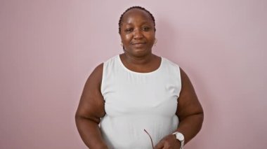 Kendinden emin, gülümseyen Afrikalı Amerikalı kadın gözlük takıyor, eğlenceli, olumlu bir hava alıyor, izole edilmiş pembe bir arka planda sıradan duruyor..