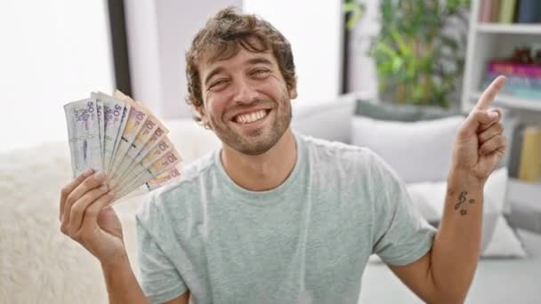 Joven Alegre Casa Sosteniendo Pesos Colombianos Señalando Con Confianza Costado — Vídeo de stock