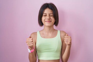 Pembe arka planda duran genç kız başarı için heyecanlanıyor kolları havada ve gözleri kapalı zaferi kutlarken gülümsüyor. Kazanan konsept. 