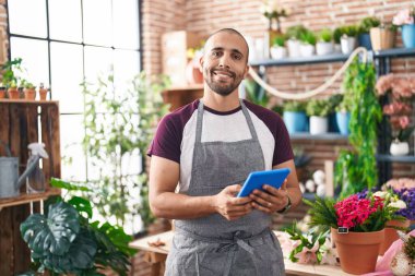 Young latin man florist smiling confident using touchpad at flower shop
