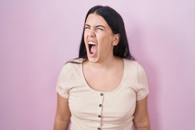 Genç İspanyol kadın pembe arka planda kızgın ve kızgın bağırıyor sinirli ve öfkeli, öfkeyle bağırıyor. öfke ve agresif konsept. 