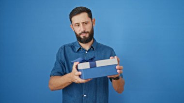 Genç İspanyol adamın elinde bir hediye var. Mavi arka planda üzgün görünüyor.