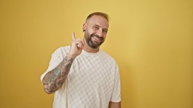 Yakışıklı genç adam, düşüncelere dalmış ve izole edilmiş sarı bir arka plana hafifçe gülümsüyor, bir fikir uyandırıyor.!