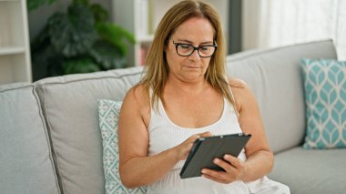 Orta yaşlı İspanyol kadın evdeki koltukta oturuyor.