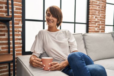 Genç ve güzel İspanyol kadın evdeki kanepede oturup kahve içiyor.