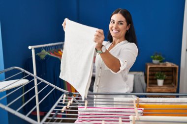 Genç ve güzel İspanyol kadın gülümsüyor çamaşırhanede çamaşır ipine asılan kendine güvenen kıyafetler.