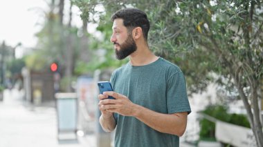 Genç İspanyol bir adam parkta akıllı telefon kullanıyor.