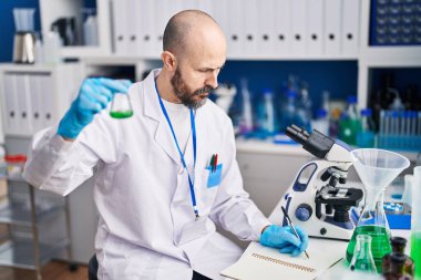 Laboratuvarda not defterine test tüpü yazan kel bir bilim adamı.