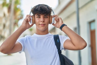 Latin kökenli genç bir öğrenci sokakta müzik dinlerken kendinden emin gülümsüyor.