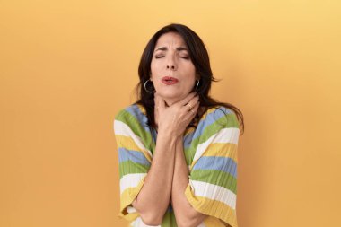 Orta yaşlı İspanyol kadın sarı arka planda durup bağırıyor ve boğuluyor çünkü acı verici bir boğulma. Sağlık problemi. Boğulma ve intihar konsepti. 