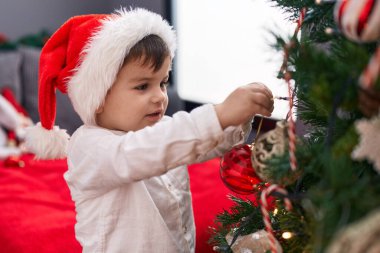 Sevimli İspanyol bebek gülümseyerek evde kendine güvenen bir Noel ağacı süsler.