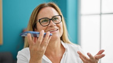 Orta yaşlı İspanyol iş kadını. Ofiste çalışan akıllı telefondan sesli mesaj gönderiyor.