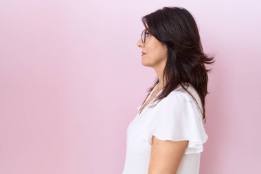 Orta yaşlı İspanyol kadın, günlük beyaz tişört ve gözlük takıyor. Taraf arıyor, rahat profil pozu veriyor. Doğal bir yüzü ve kendine güvenen bir gülümsemesi var.. 
