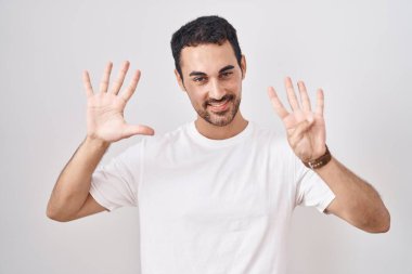 Beyaz arka planda duran yakışıklı İspanyol adam dokuz numarayı gösterip işaret ederken kendinden emin ve mutlu gülümsüyor.. 