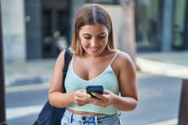 Young beautiful hispanic woman student smiling confident using smartphone at street