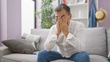Depresyonda olan, gri saçlı, yoğun stres altında, evde yalnız, oturma odasındaki kanepede oturan, duygularıyla savaşan bir İspanyol.