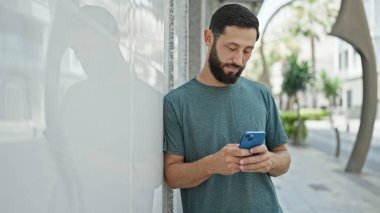 Genç İspanyol adam akıllı telefon kullanıyor. Sokakta ciddi bir ifadesi var.
