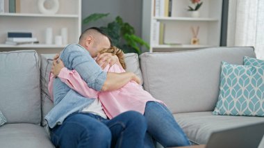 Erkek ve kadın çift evdeki kanepede oturup birbirlerine sarılıyorlar.