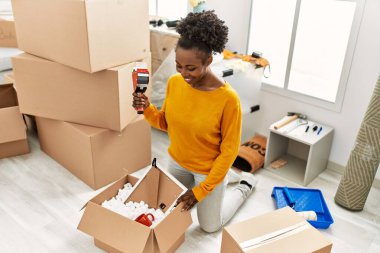 Afro-Amerikalı kadın yeni evinde kendine güvenen bir karton kutu paketliyor.