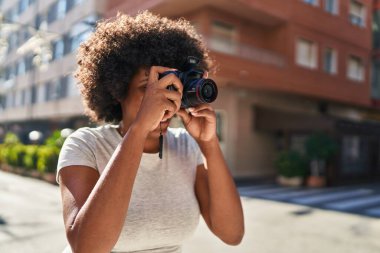 Sokakta profesyonel kamera kullanan Afro-Amerikan kadın gülümsüyor.