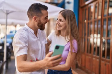 Man and woman couple smiling confident using smartphone at street