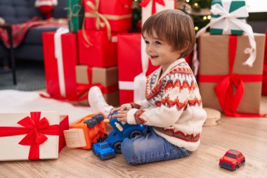 Adorable toddler playing with truck toy sitting on floor by christmas tree at home