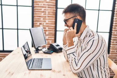 Genç İspanyol iş adamı. Ofiste bilgisayarla akıllı telefondan konuşuyor.