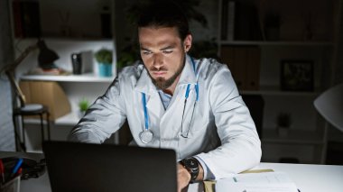 Genç İspanyol doktor klinikte çalışırken dizüstü bilgisayar kullanıyor.