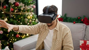 Genç Arap adam sanal gerçekliği kullanıyor. Evde Noel ağacının yanında oturuyor.
