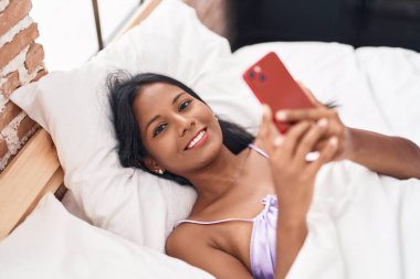 Genç ve güzel bir kadın yatak odasında akıllı telefon kullanıyor.