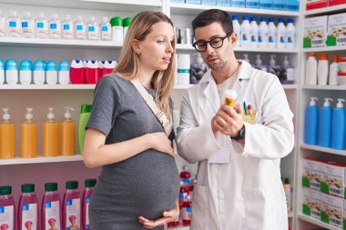 Kadın ve erkek eczacı ve hamile müşteri eczanede ilaç şişesi tutuyorlar.