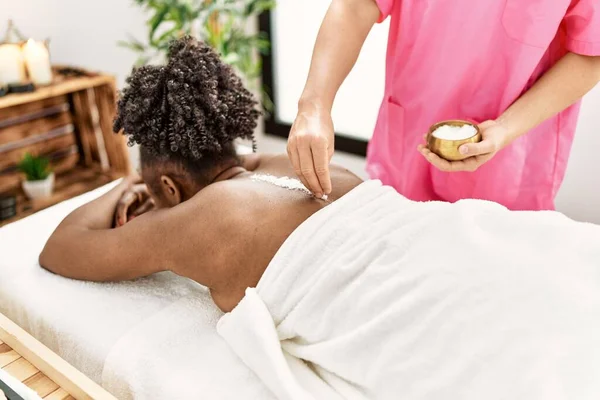 African american woman lying on table having back massage using salt at beauty salon
