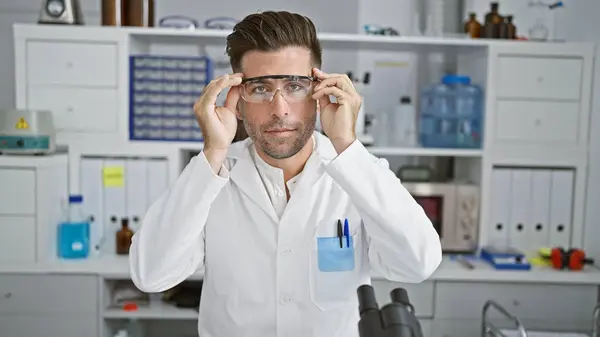 Young hispanic man scientist wearing security glasses with serious face at laboratory