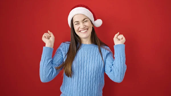 年轻的高加索女人 头戴圣诞帽 手臂高举在孤立的红色背景之上 — 图库照片