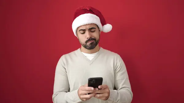 Young Hispanic Man Wearing Christmas Hat Using Smartphone Unhappy Expression — Stock Photo, Image