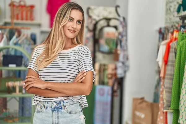 Young blonde woman customer smiling confident standing with arms crossed gesture at clothing store
