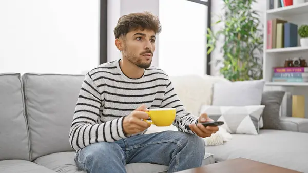Young arab man watching television drinking coffee at home